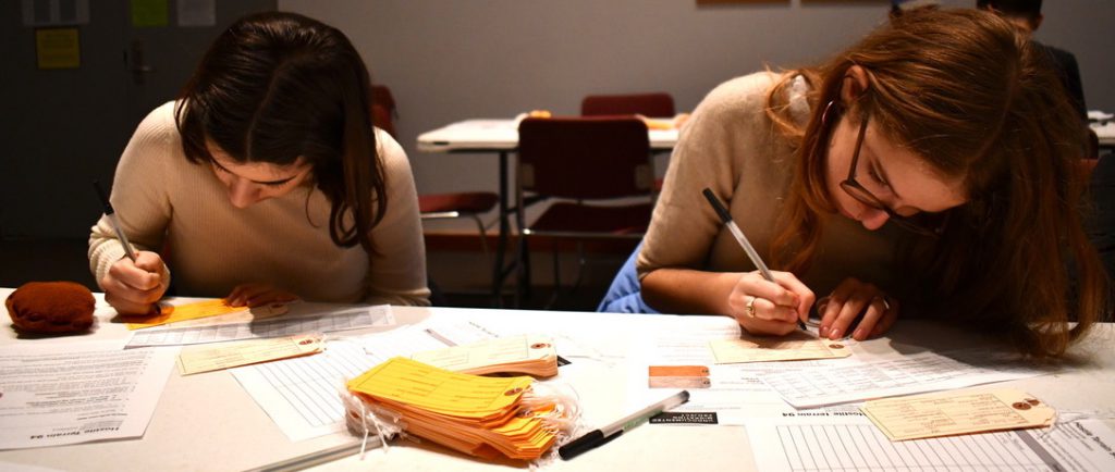 two people leaning closely over a table while filling out toe tags for the HT94 project