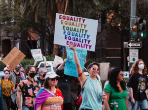 Women marching, holding up sign that repeats, "Equality."